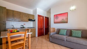 A kitchen with wooden cabinets, a dining table with chairs, a sofa, and a wall-mounted light fixture. - Apartment 'Rosa's' with Sea View and Private Terrace (Isola Rossa)