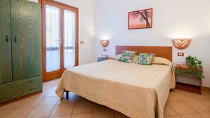 A bedroom with a bed, a wardrobe, a nightstand, a wall-mounted lamp, and a picture of a palm tree. - Apartment 'Rosa's' with Sea View and Private Terrace (Isola Rossa)
