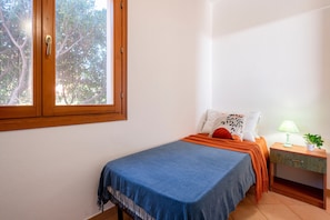 A bedroom with a bed, a nightstand, a lamp, and a window with a view of trees.