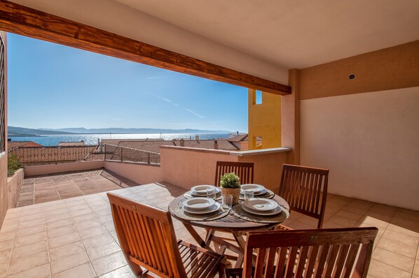 A terrace with a table set for dining, a potted plant, and a view of the sea and mountains.
