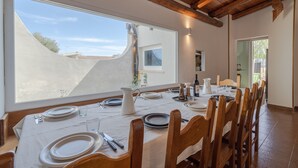 Un coin repas avec une table dressée pour six personnes, de grandes fenêtres et des poutres en bois au plafond.