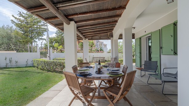 Une terrasse extérieure avec une table ronde dressée pour le repas, entourée de chaises en bois.