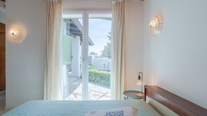Une chambre à coucher avec un lit, des rideaux, une table de chevet et une vue sur l’extérieur.