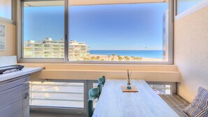 A balcony with a view of the beach and ocean, a dining table with chairs, and a small seating area with a patterned cushion. - Studio Apartment 'Vue Mer' with Sea View, Wi-Fi and Air Conditioning (Canet-en-Roussillon)
