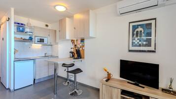 Cocina compacta con microondas, lavamanos y taburetes de bar. Se ve un televisor de pantalla plana y un mueble pequeño.
