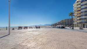 A wooden boardwalk with benches, a bicycle, and a beach in the background. - Studio Apartment 'Vue Mer' with Sea View, Wi-Fi and Air Conditioning (Canet-en-Roussillon)
