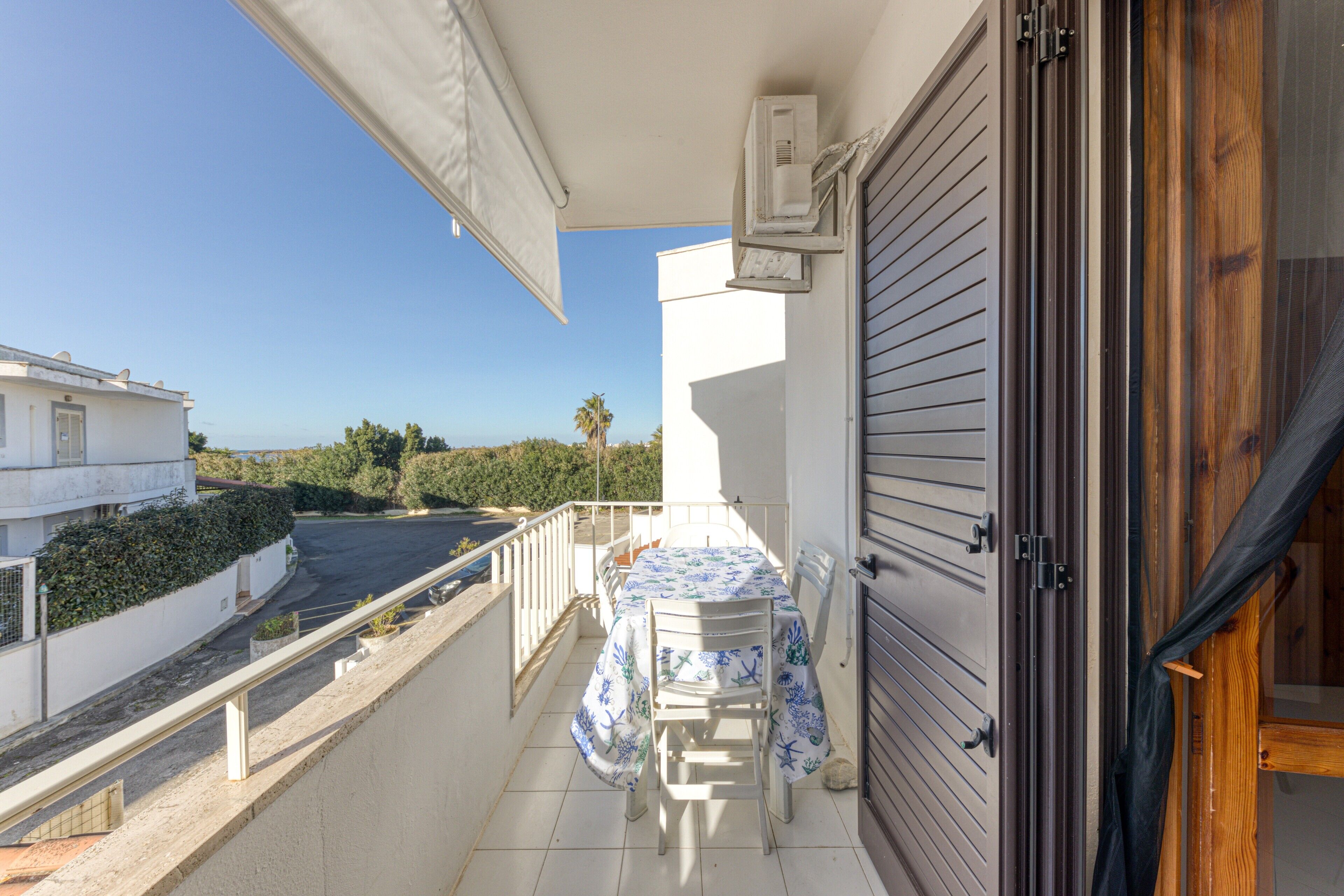 Un balcon avec une table et des chaises, une vue sur la rue et un immeuble en arrière-plan.