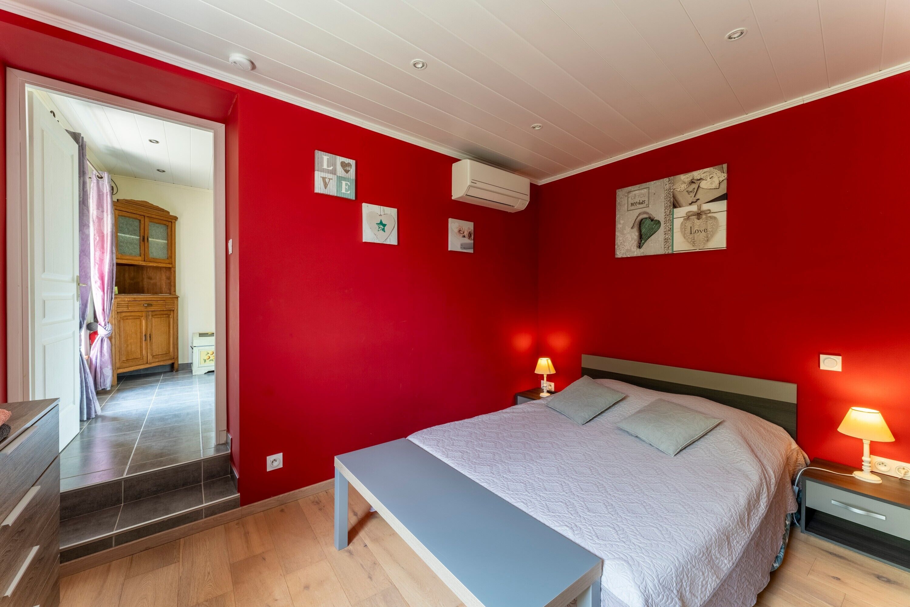 Une chambre à coucher comprenant un lit, des tables de chevet, un banc, une armoire et un miroir.