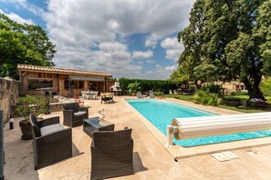 A poolside area with wicker furniture, a swimming pool, and a building with a tiled roof.