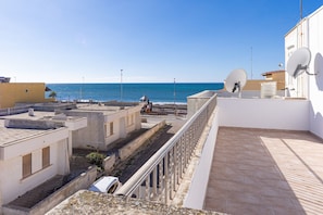 A rooftop terrace with a view of the sea, satellite dishes, and a building with a flat roof.