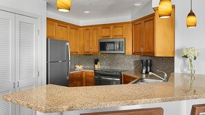 Cocina con gabinetes de madera, encimeras de granito, electrodomésticos de acero inoxidable e iluminación colgante.