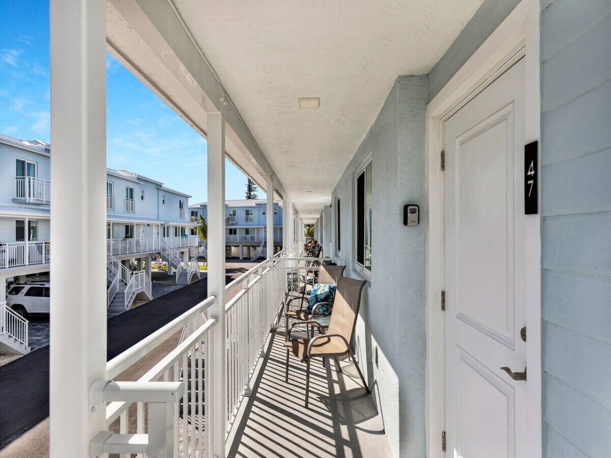 A covered balcony with a railing, a door, and a view of neighboring buildings.