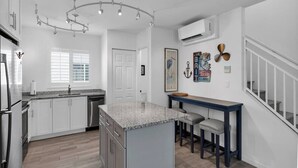 A modern kitchen with white cabinets, a granite countertop, and a central island with bar stools. - Best Catch on Grouper LN at Ocean Isles (Marathon)