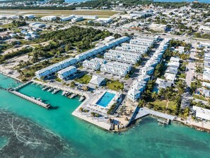 An aerial view of a coastal resort with multiple buildings, a marina, and a swimming pool.
