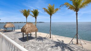A beachside deck with palm trees and thatched umbrellas, overlooking the sea. - Best Catch on Grouper LN at Ocean Isles (Marathon)