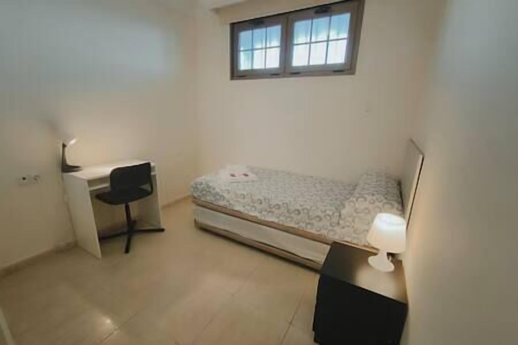 Een klein appartement met één kamer, een bed, een bureau en een stoel.