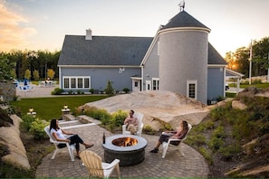 A house with a circular tower, a fire pit, and outdoor seating.