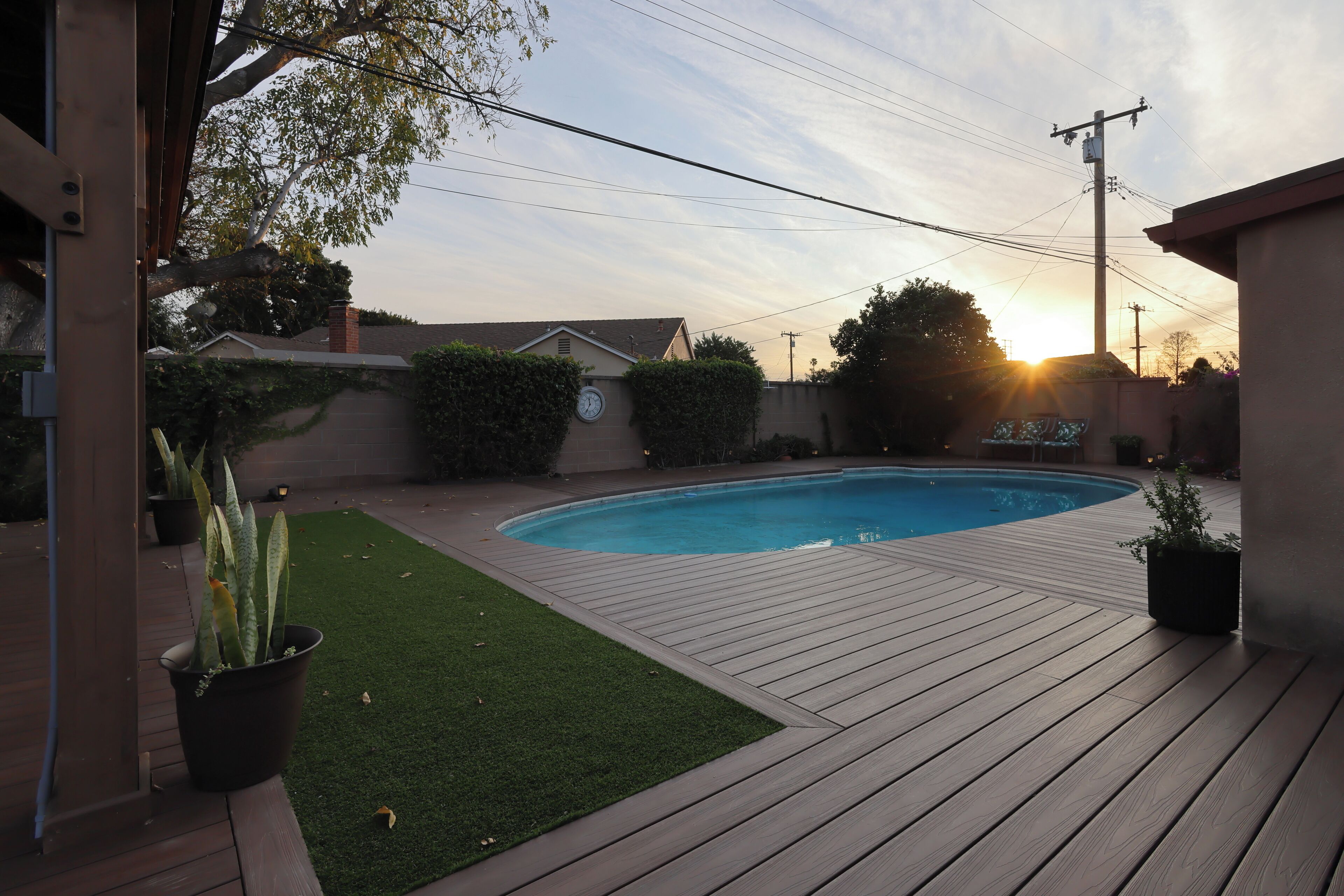A backyard with a wooden deck, a swimming pool, and a small patch of artificial grass.