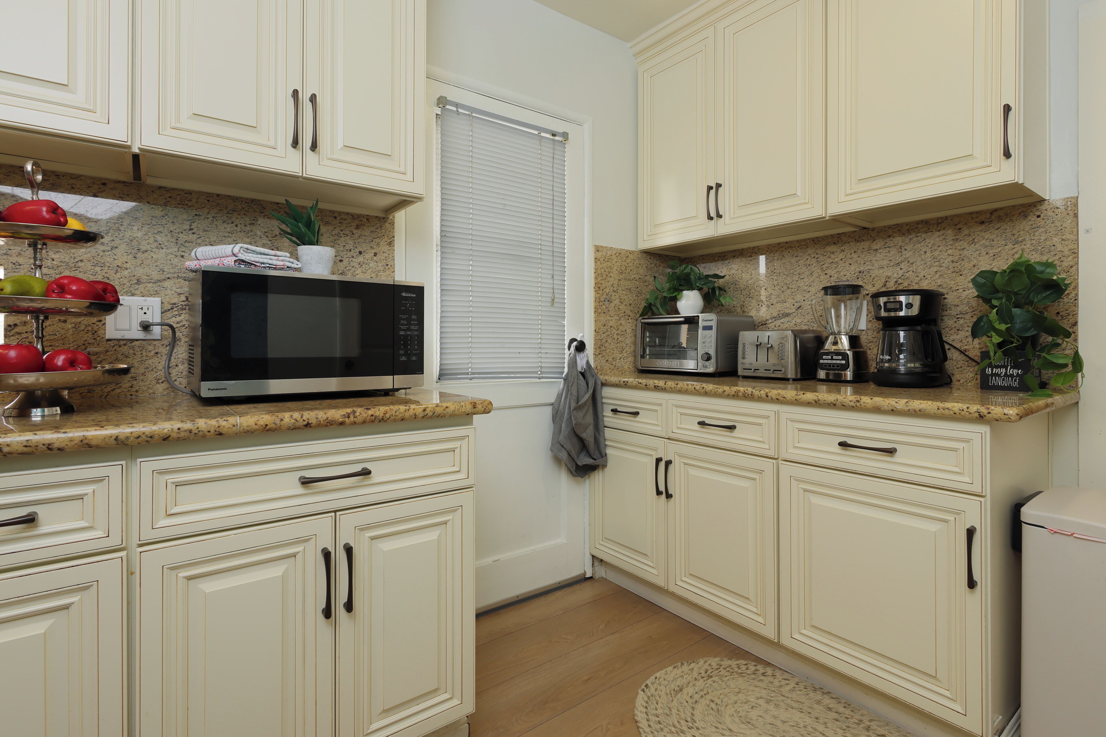 A kitchen with white cabinets, a microwave, a coffee maker, and a potted plant.