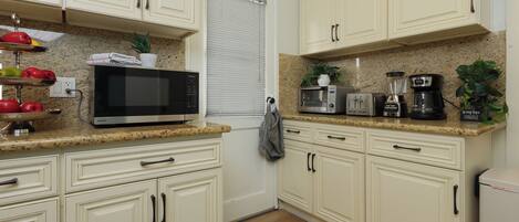 A kitchen with white cabinets, a microwave, a coffee maker, and a potted plant.
