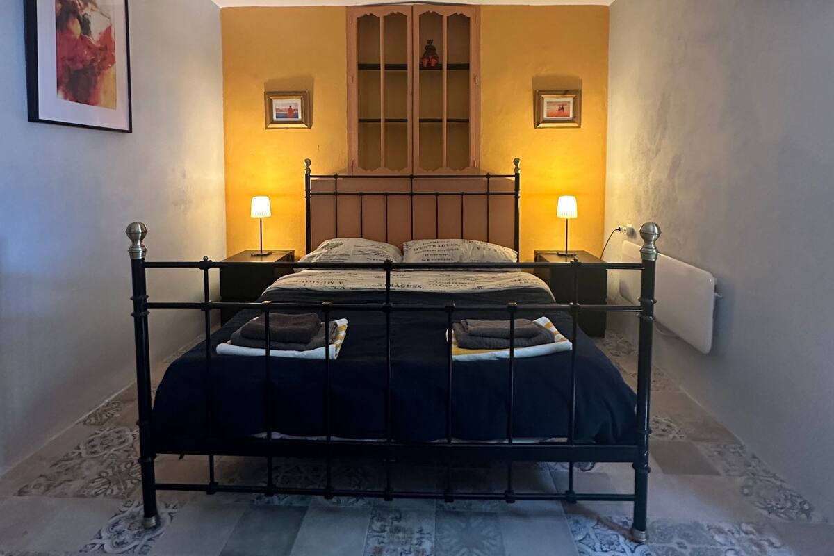 A bedroom with a bed, two bedside lamps, a ceiling fan, and a cabinet above the bed.