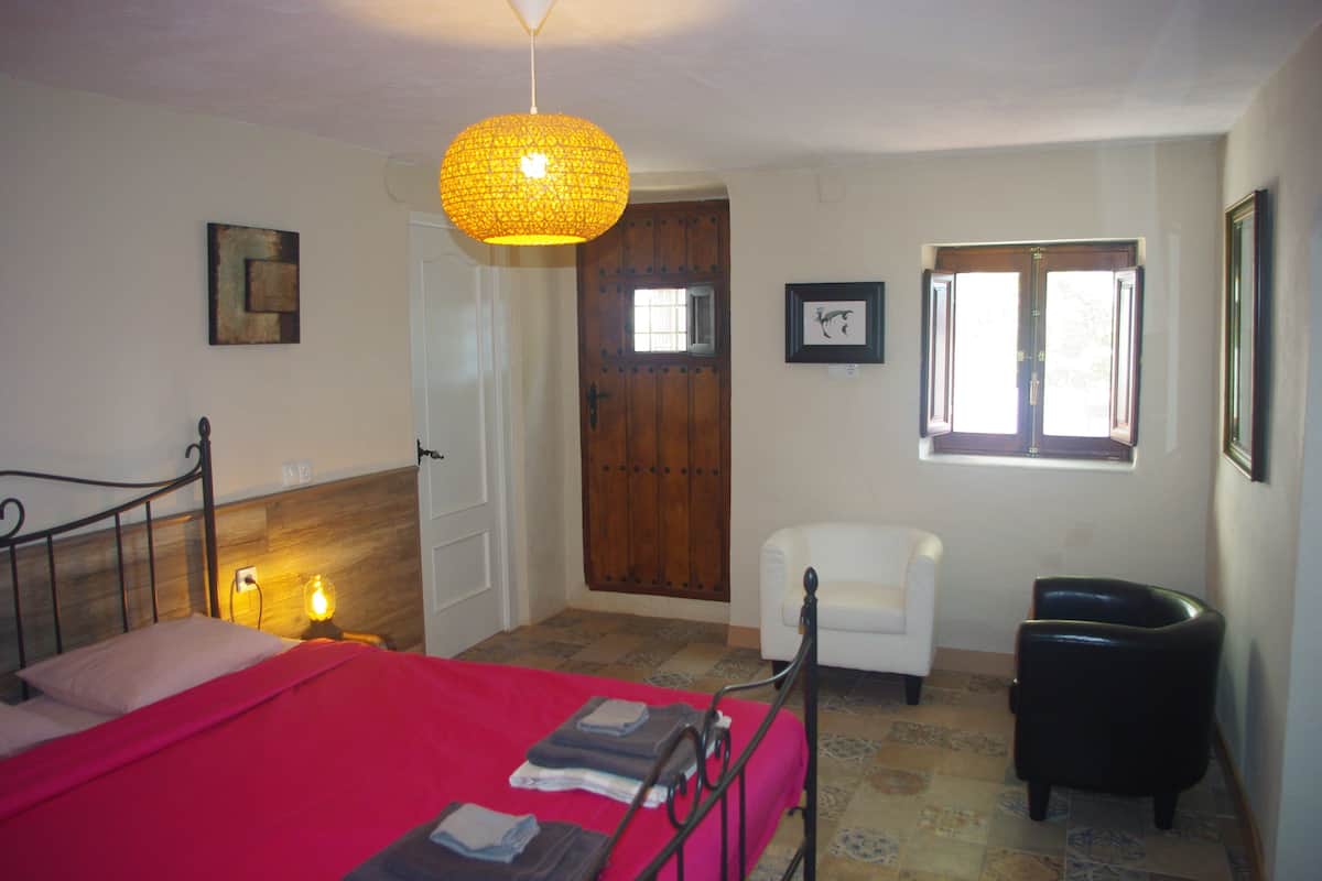 A bedroom with a bed, a chair, a desk, a door, and a window.