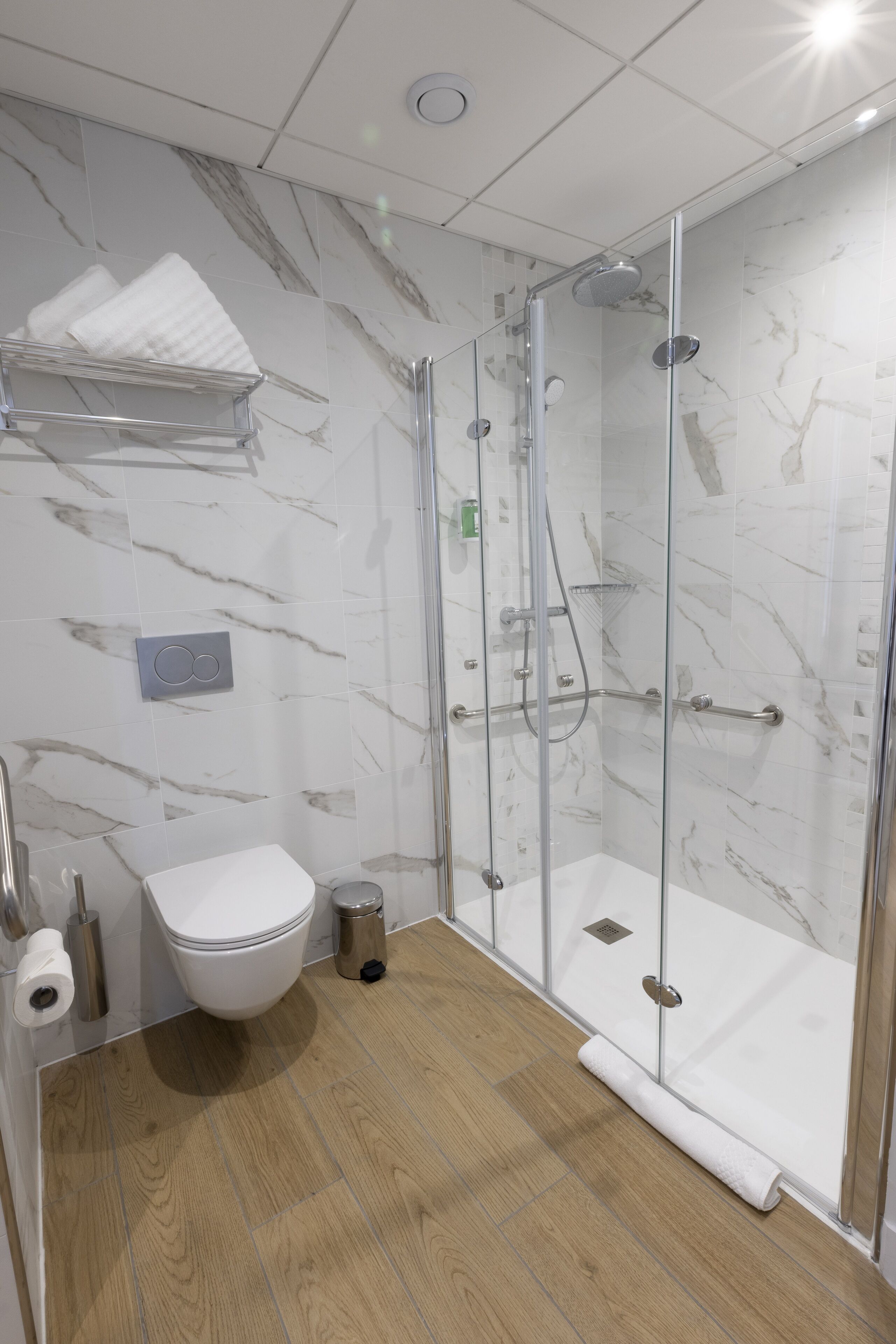 A modern bathroom with a glass-enclosed shower, a toilet, and a towel rack.