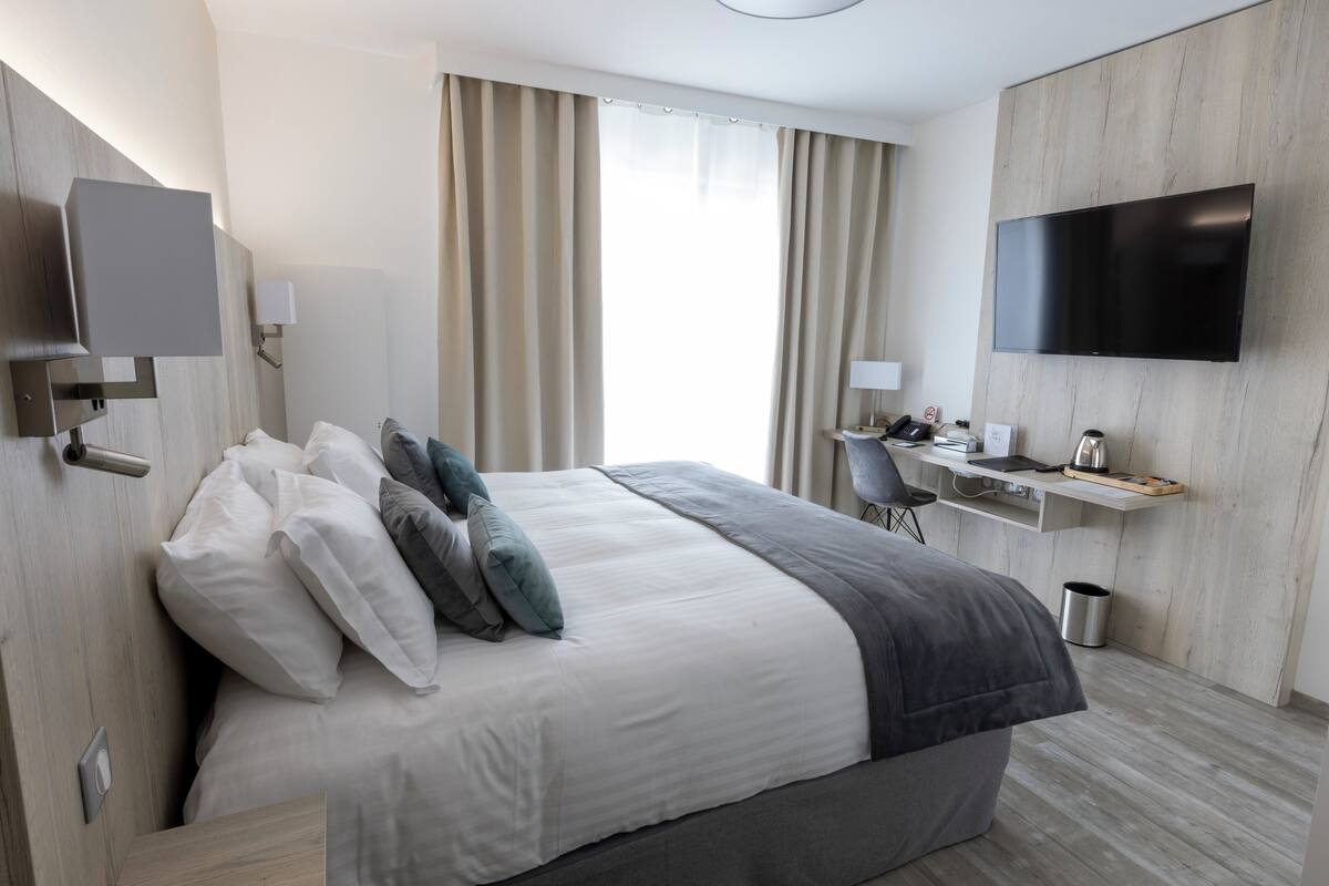 A modern hotel room with a large bed, a desk with a chair, a flat-screen TV, and a window with curtains.