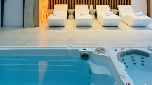 Area piscina interna moderna con sedie a sdraio e vasca idromassaggio.