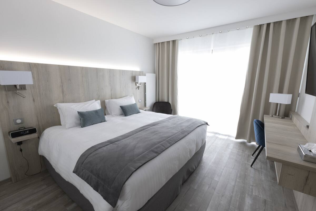 A modern hotel room with a large bed, bedside tables, a desk, and a chair.