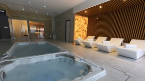 Un'area spa moderna con due vasche idromassaggio, poltrone relax e una parete in legno.