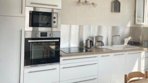 A kitchen with white cabinets, a microwave, an oven, a coffee maker, and a sink. - L'océane du pays - Saint hilaire de Riez (SAINT HILAIRE DE RIEZ)