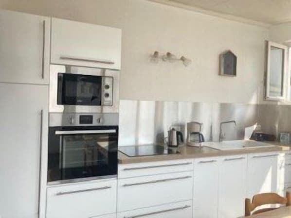 A kitchen with white cabinets, a microwave, an oven, a coffee maker, and a sink. - L'océane du pays - Saint hilaire de Riez (SAINT HILAIRE DE RIEZ)