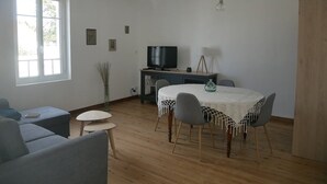 A spacious living room with a round table, two sofas, a television, and a large window. - L'océane du pays - Saint hilaire de Riez (SAINT HILAIRE DE RIEZ)