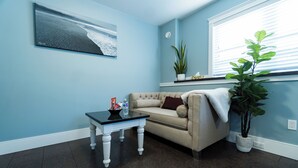 A living room with a beige sofa, a small table with a bottle and a bowl, a potted plant, and a wall-mounted picture.