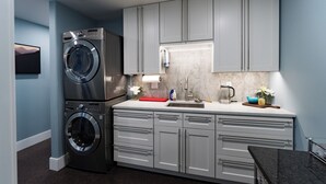 A modern kitchen with grey cabinets, a built-in washing machine, and a marble countertop.