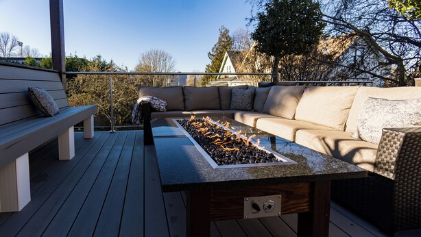 An outdoor deck with a glass-top table, a fire feature, a sofa, and a bench.