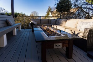 Una terraza al aire libre con una mesa de vidrio, un hogar para fuego, un sofá y un banco.