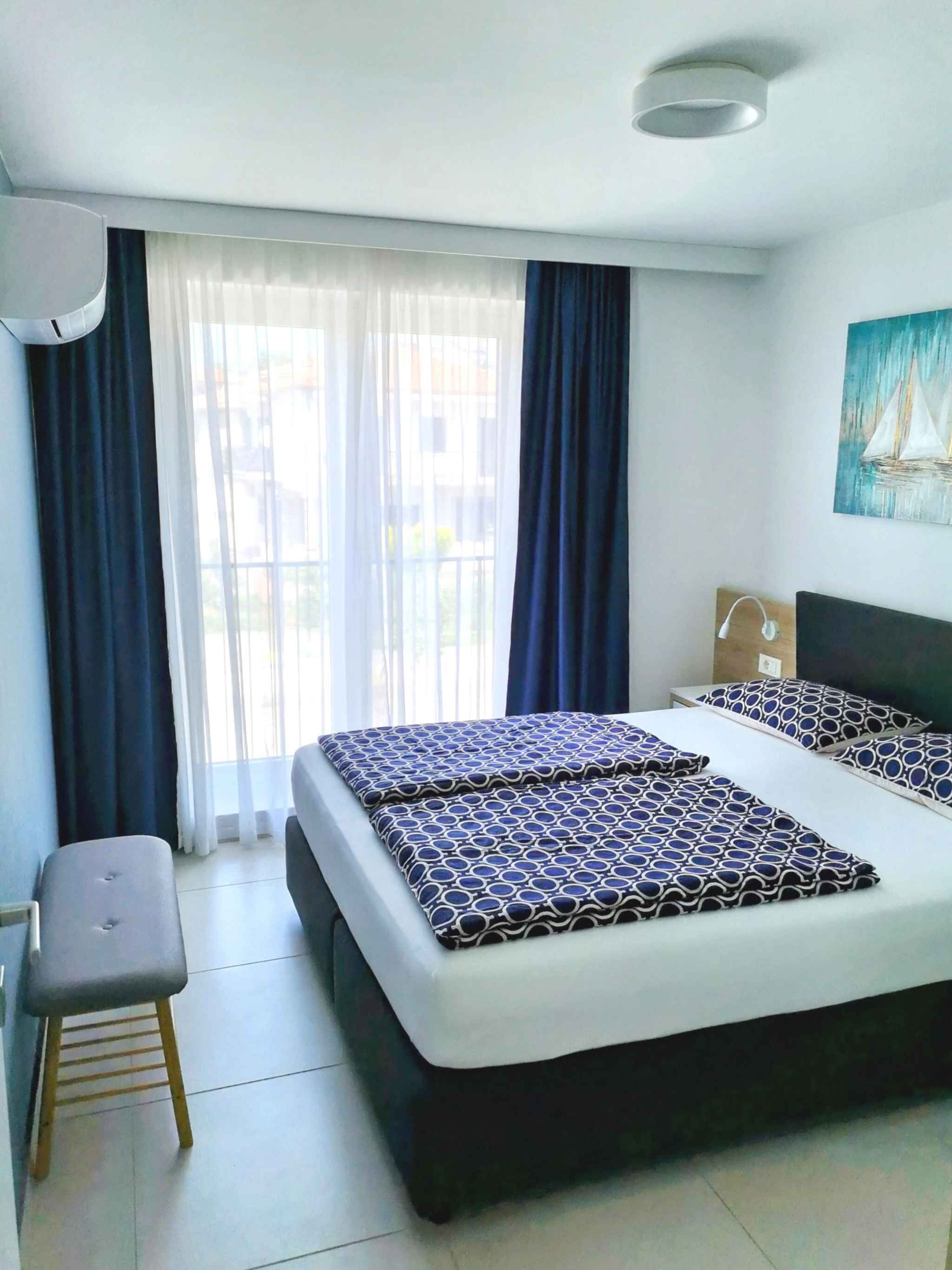 A modern bedroom with a large bed, a bench, and a window with curtains.