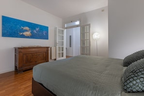 Una camera da letto con un letto, una cassettiera, un quadro e una porta che dà su un'altra stanza.