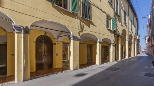 Ein gelbes Gebäude mit Bogenfenstern und grünen Fensterläden, eine gepflasterte Straße und ein klarer Himmel.