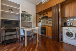 A compact kitchen with a microwave, oven, and washing machine. There is a dining area with a table and chairs. - GuestHost - Bright studio apartment perfect for two people, located in a building with a garden in the Cirenaica district, an area near the center equipped with all services. Located just 20 meters from the entrance to the S.Orsola Polyclinic, it is idea (Bologna)