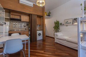 A compact living space with a kitchenette, a dining area, a sofa, and a washing machine. - GuestHost - Bright studio apartment perfect for two people, located in a building with a garden in the Cirenaica district, an area near the center equipped with all services. Located just 20 meters from the entrance to the S.Orsola Polyclinic, it is idea (Bologna)