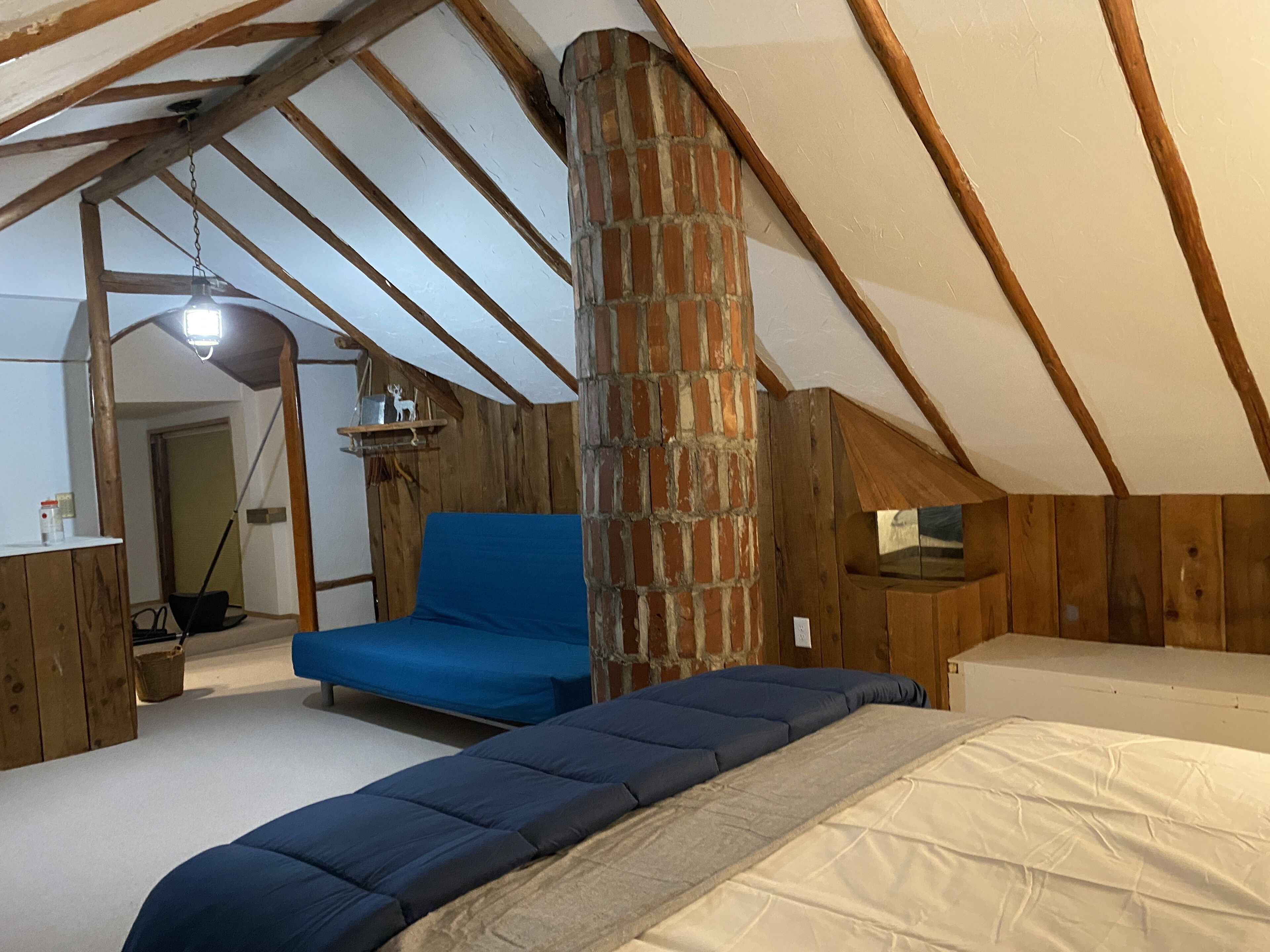 Ein Schlafzimmer im Loft-Stil mit freiliegenden Holzbalken, einem Backsteinofen und einem blauen Sofa.