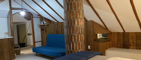 Ein Schlafzimmer im Loft-Stil mit freiliegenden Holzbalken, einem Backsteinofen und einem blauen Sofa.