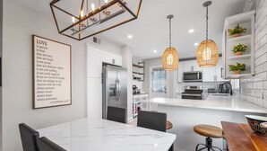 A modern kitchen with white cabinetry, a marble countertop, and pendant lighting.