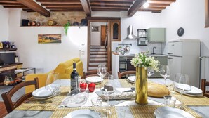 A dining area with a table set for four, a kitchen in the background, and a staircase leading to another level. - Stunning apartment in Monticchiello with WiFi (Monticchiello)