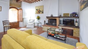 A living room with a fireplace, a television, and a bookshelf. - Stunning apartment in Monticchiello with WiFi (Monticchiello)