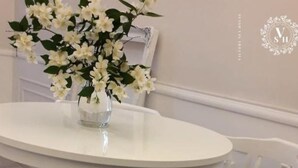 Une table ronde blanche, sur laquelle est posé un vase de fleurs blanches, est flanquée de deux chaises blanches.