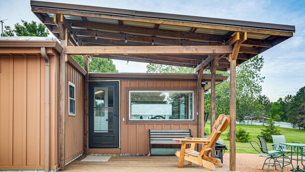 A wooden deck with a bench and a table, a covered patio area, and a view of a green landscape. - Rhinelander Vacation Rental w/ Yard on Venus Lake! (Rhinelander)